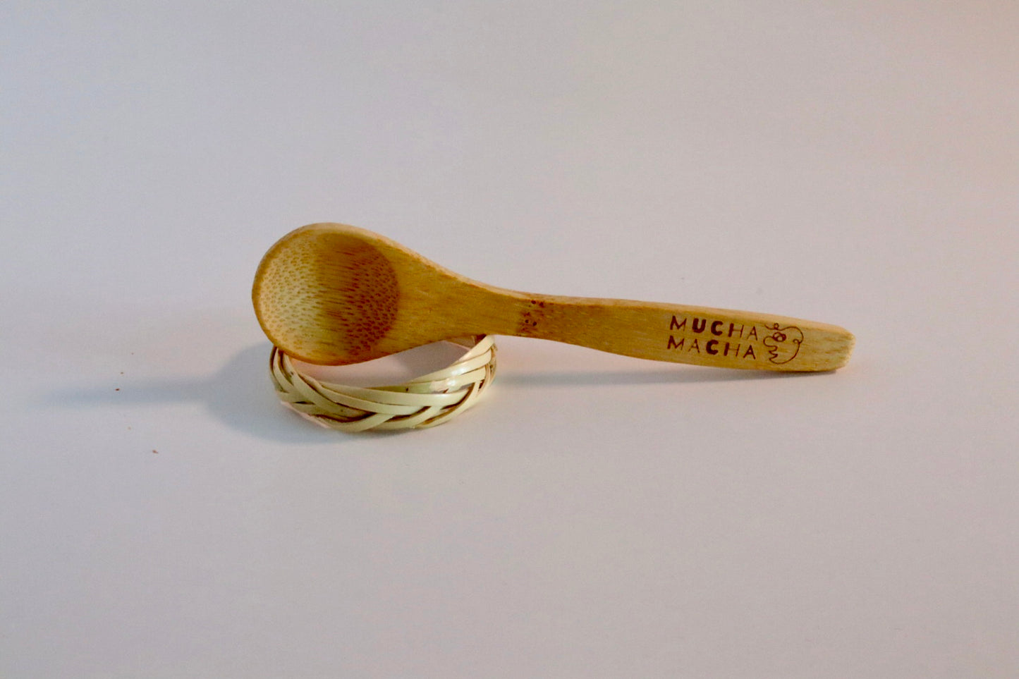 Wooden spoon with 'Mucha Macha' branding on a light gray background