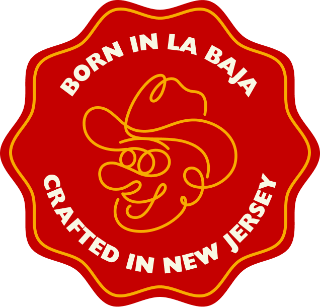 A red scalloped badge-style graphic with yellow border lines, a yellow cowboy line drawing in the center, and white text reading “BORN IN LA BAJA” and “CRAFTED IN NEW JERSEY”.
