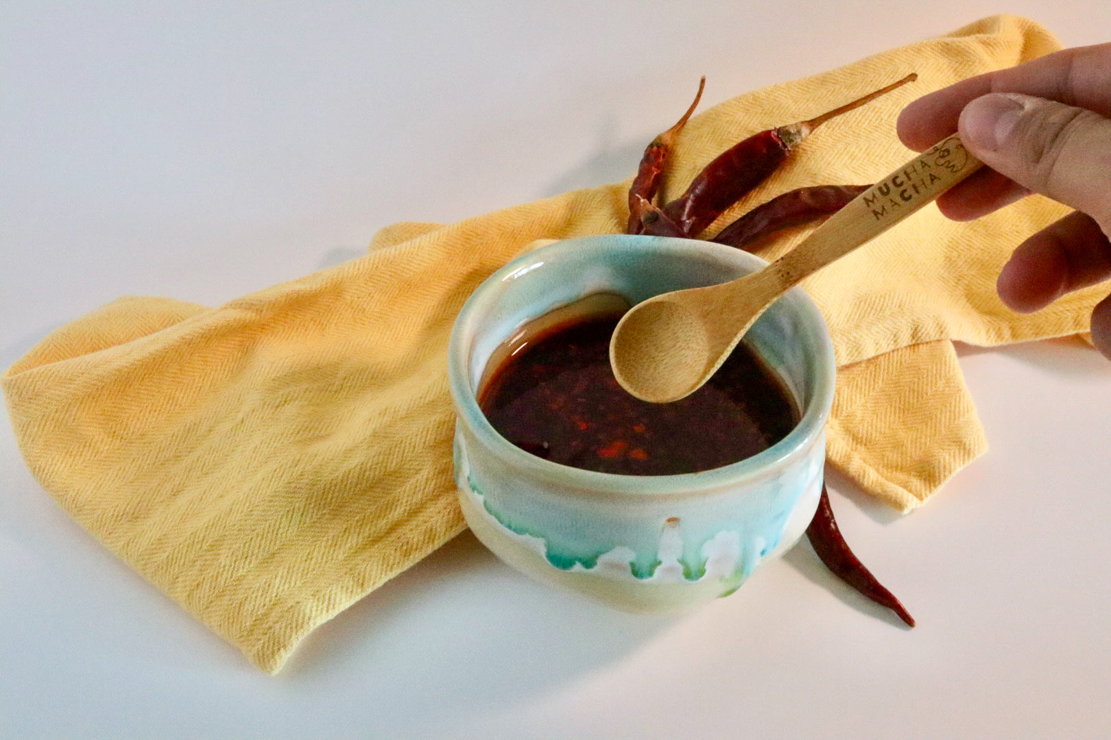Small bowl of dark sauce with a wooden spoon on a yellow cloth