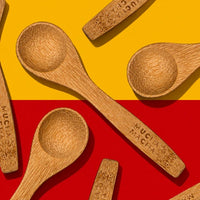 Several wooden spoons with engraved text are arranged diagonally on a split yellow and red background.