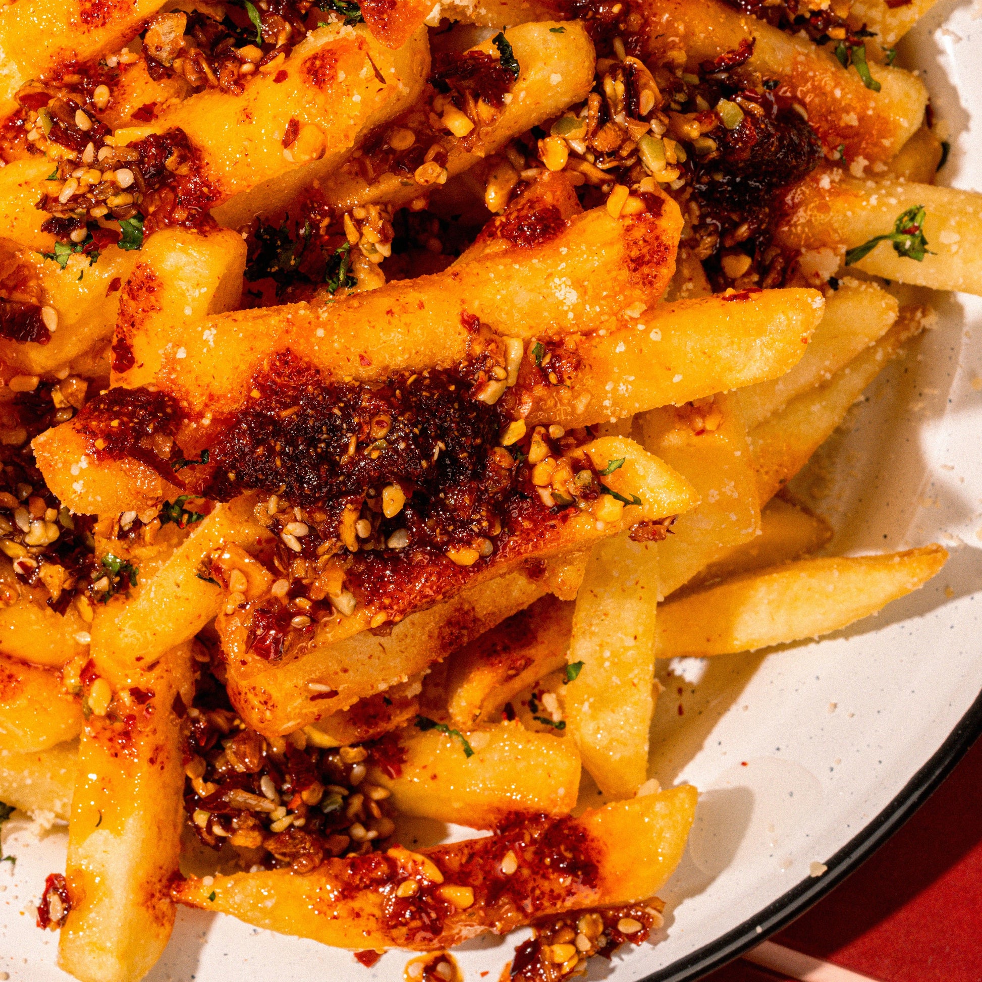 Close-up of a plate of golden french fries topped with Mucha Macha, crushed garlic, and sesame seeds.