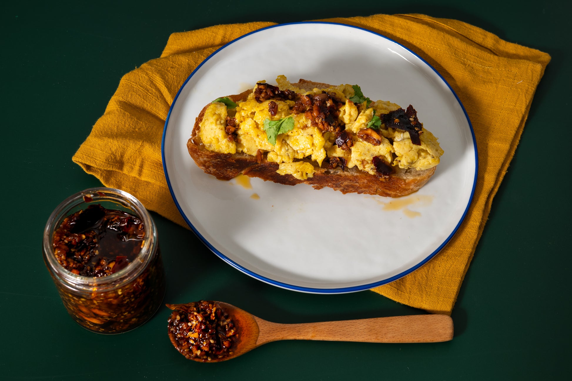 Scrambled egg on toast with a side of jam on a white plate with a yellow napkin.