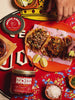 Short video loop of hands squeezing lime and topping fresh tacos with Mucha Macha salsa macha next to a product jar.